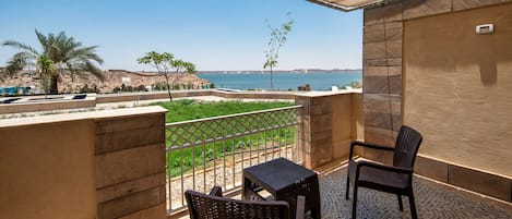 A balcony with a view of the sea, two wicker chairs, a small table, and a tiled floor.
