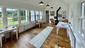 Ett rymligt rum med stora fönster, en matplats och en öppen spis.
