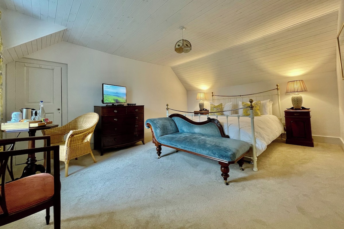 Ein Schlafzimmer mit einem Bett, einem Sessel, einem Schreibtisch, einer Kommode und einem Fernseher.
