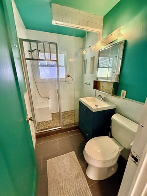 Un baño con cabina de ducha de vidrio, inodoro blanco, lavamanos y espejo.