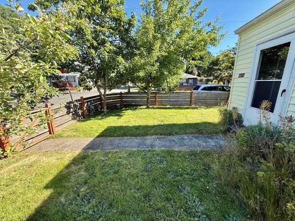 Patio trasero residencial con cerca de madera, un árbol y una casa con un número visible.