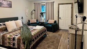 Une pièce confortable avec un lit, deux fauteuils, une petite table, une lampe, un miroir et une porte.