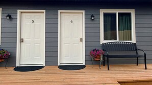 Une maison avec deux portes blanches portant les numéros 5 et 6, un banc et des plantes en pot sur le porche.