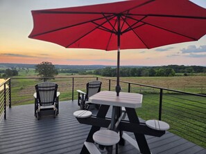 Una terraza con una mesa y sillas, un paraguas rojo y vista a un campo.