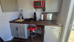 A compact kitchen with a microwave, coffee maker, and two stools. - Tiny Home with Rooftop Deck (Pikeville)