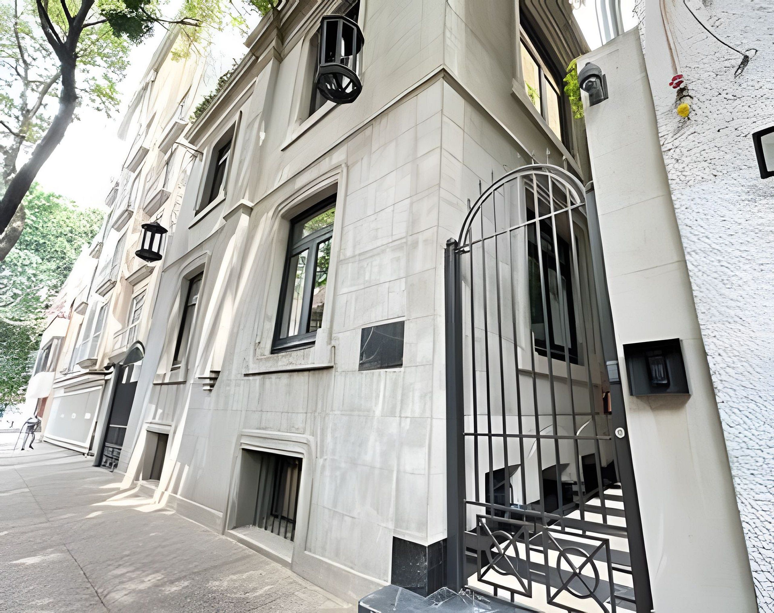 A building with a large entrance gate, multiple windows, and a paved sidewalk.