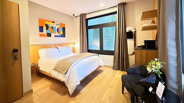 A hotel room with a bed, a chair, a desk, a window with curtains, and a wall art piece. - Modern Suite 3 - Heart of Roma Norte (Mexico City)