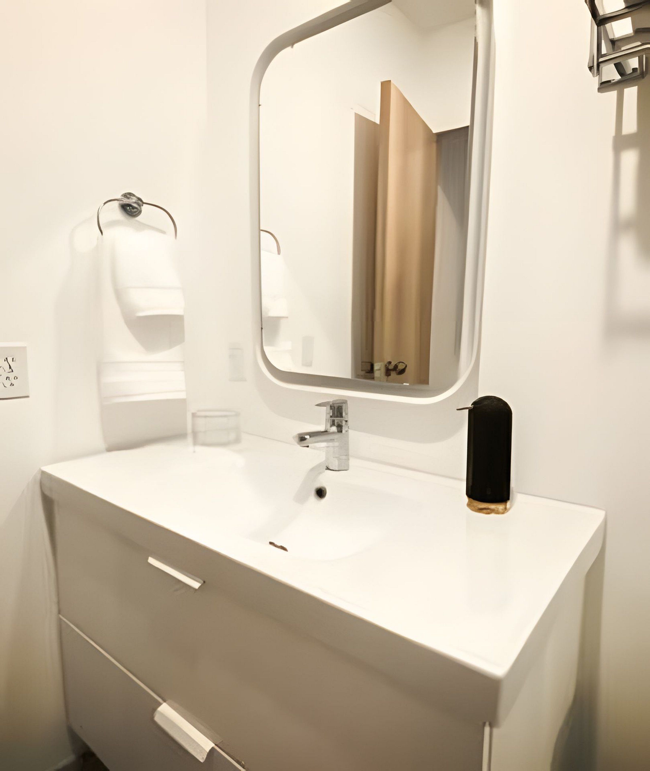 Ein modernes Badezimmer mit einem weißen Waschtisch, einem Spiegel und einem schwarzen Seifenspender.