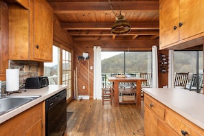Cozinha de cabana de madeira com teto de madeira, mesa de jantar com cadeiras e vista para as montanhas através de grandes janelas.