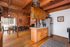 Interior em madeira com cozinha, mesa de jantar e cadeiras.
