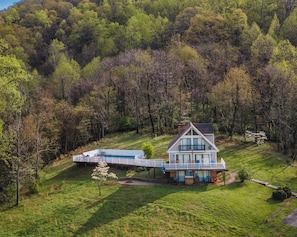 Uma casa de dois andares com varanda, cercada por uma paisagem verdejante e uma floresta densa.