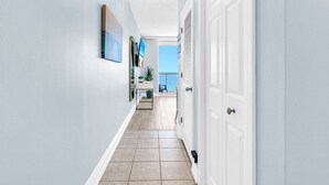 A hallway with a white door, a small table with a plant, and a view of the outside. - New Majestic BeachFront -Indoor pool, Starbucks (Panama City Beach)