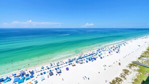 A beach with white sand, clear turquoise water, and numerous blue umbrellas. - New Majestic BeachFront -Indoor pool, Starbucks (Panama City Beach)