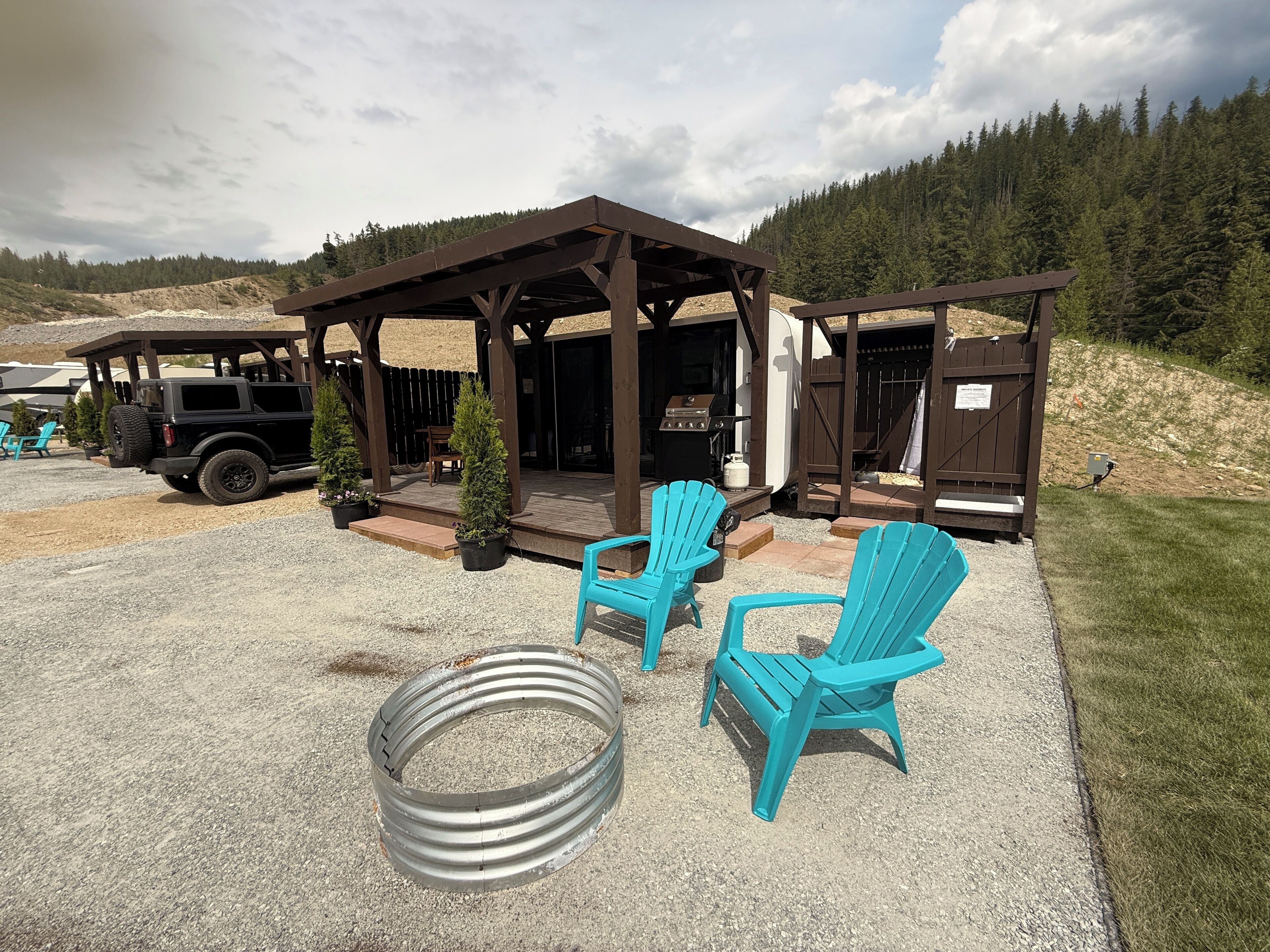 A covered outdoor area with two blue Adirondack chairs, a barbecue grill, and a Jeep parked nearby.