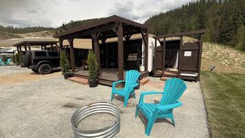 A covered outdoor area with two blue Adirondack chairs, a barbecue grill, and a Jeep parked nearby.
