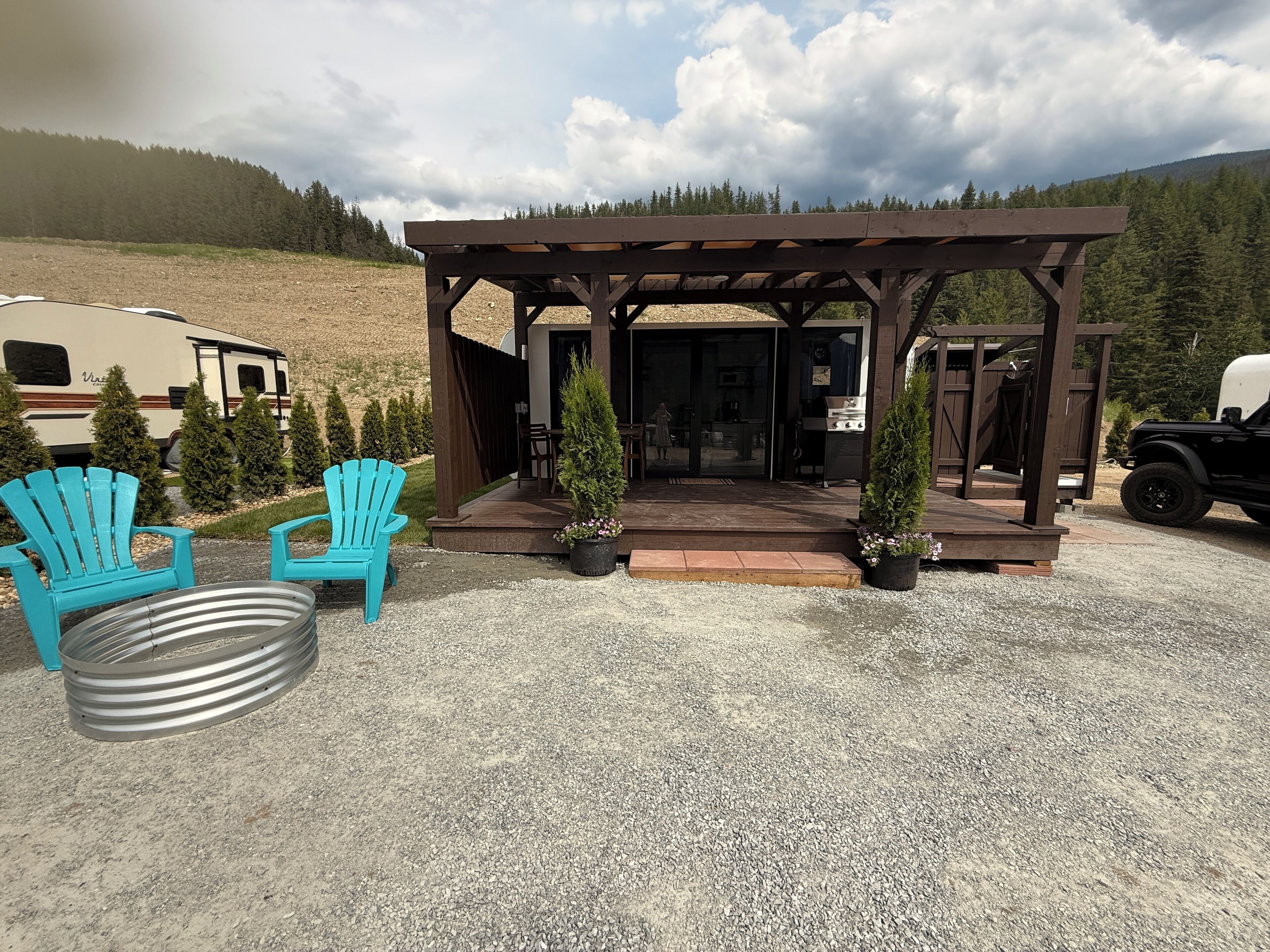 A gazebo with a gravel ground, two turquoise Adirondack chairs, and a grill area.