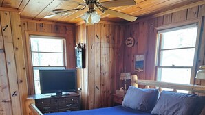 Un dormitorio de cabaña de madera con una cama, un televisor y un ventilador de techo.