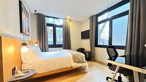 Ein Hotelzimmer mit Bett, Schreibtisch, Stuhl und großen Fenstern.