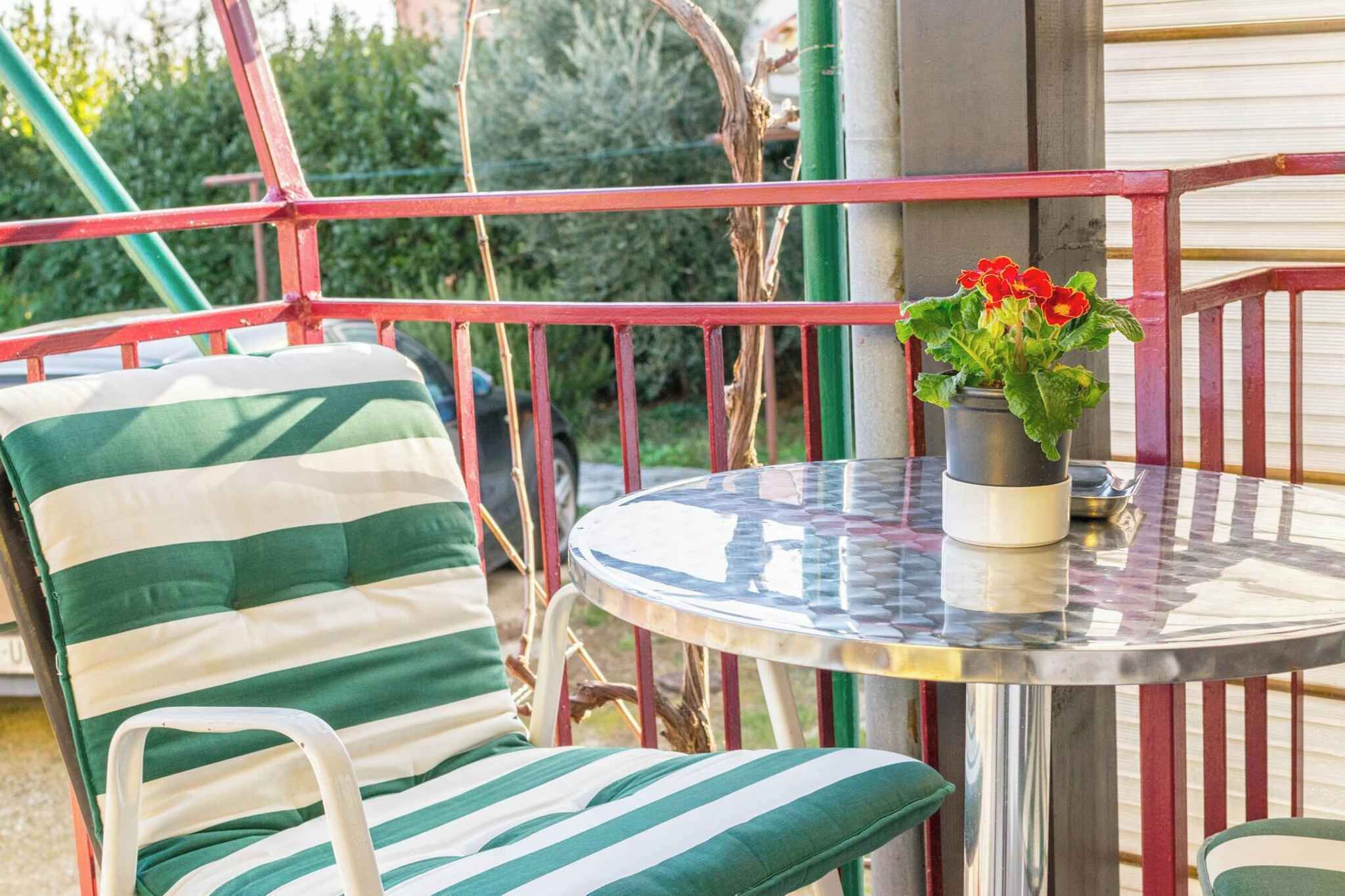 A balcony with a striped chair, a small table, and a potted plant with red flowers.