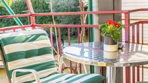 A balcony with a striped chair, a small table, and a potted plant with red flowers.