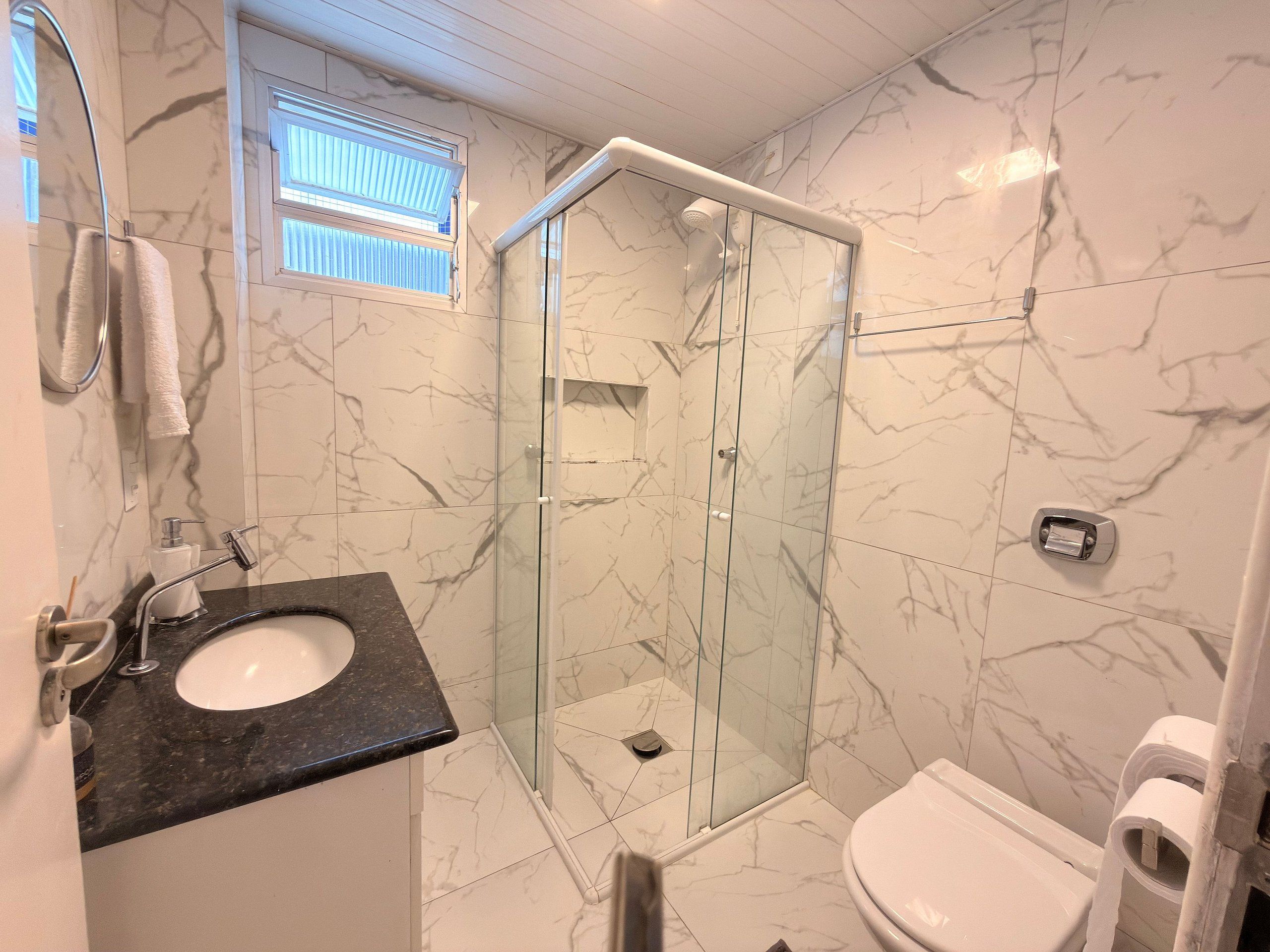A bathroom with a glass-enclosed shower, a sink with a marble countertop, and a toilet.