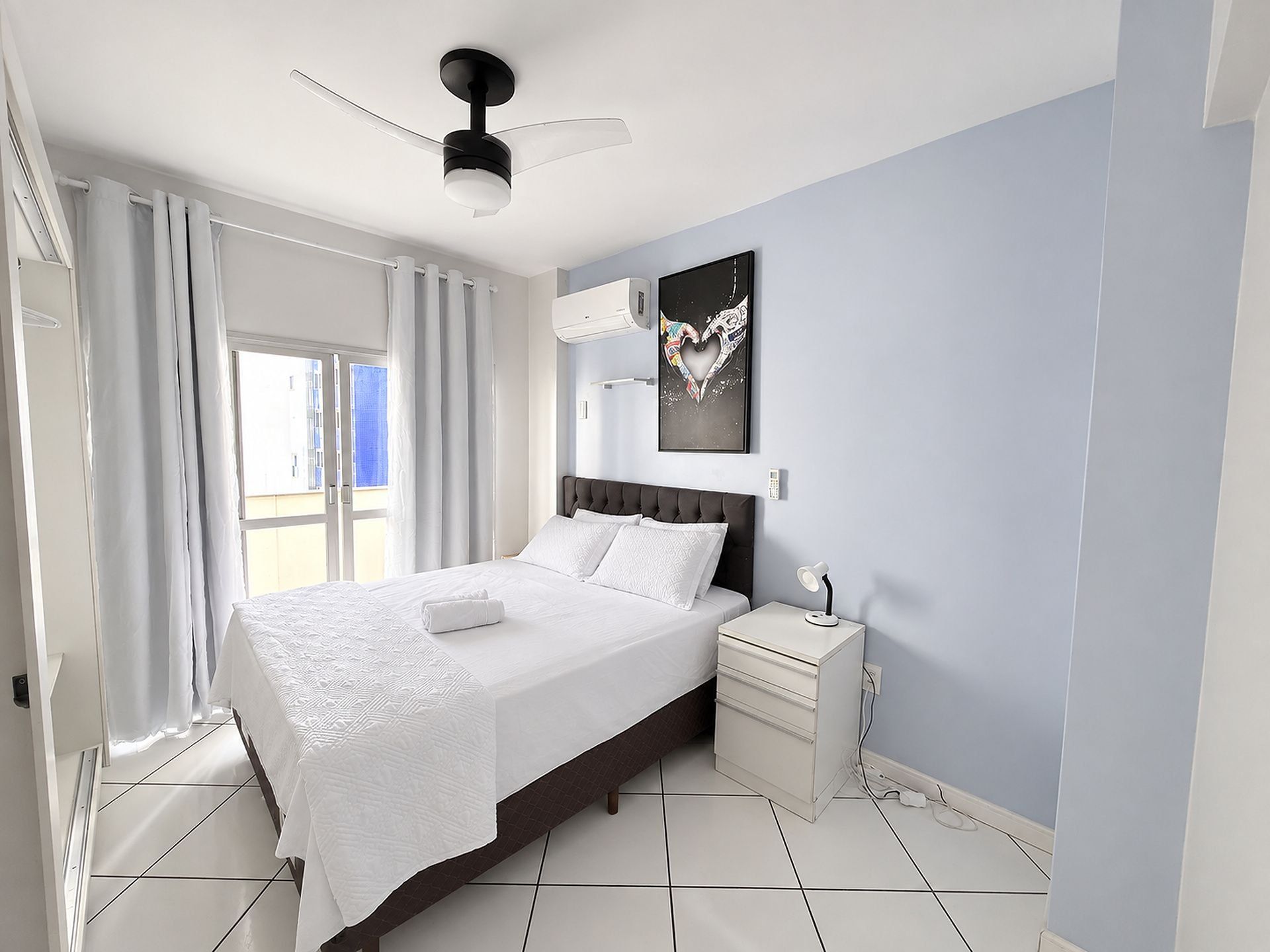 Un dormitorio con una cama, una mesita de noche, aire acondicionado de pared y ventilador de techo.