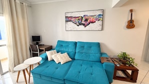 A living room with a teal sofa, a small white table, a TV, a guitar, and a painting on the wall. - Republica Argentina (Balneário Camboriú)