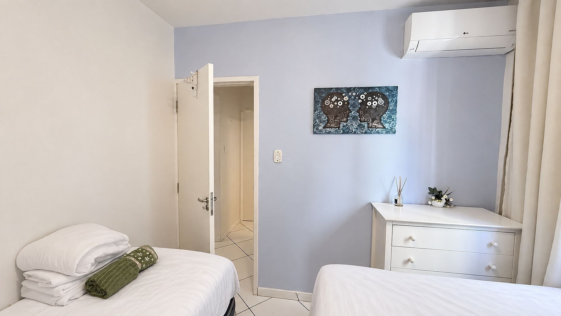 Habitación de hotel con dos camas, una mesita de noche con lámpara, aire acondicionado instalado en la pared y un cuadro.