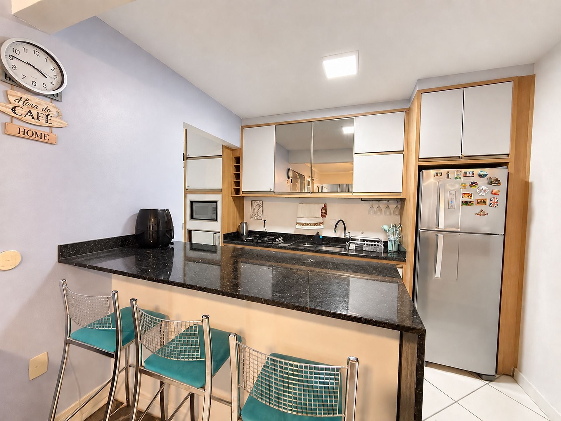A compact kitchen with a refrigerator, microwave, and a coffee maker on the counter. There are two chairs with mesh backs and teal cushions.