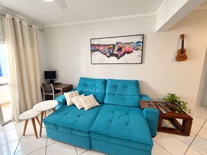 A living room with a teal sofa, a small white table, a TV, a guitar, and a painting on the wall. - Republica Argentina (Balneário Camboriú)