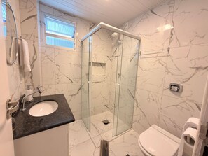 Une salle de bain avec une douche à parois de verre, un lavabo doté d’un plan de toilette en marbre et des toilettes.