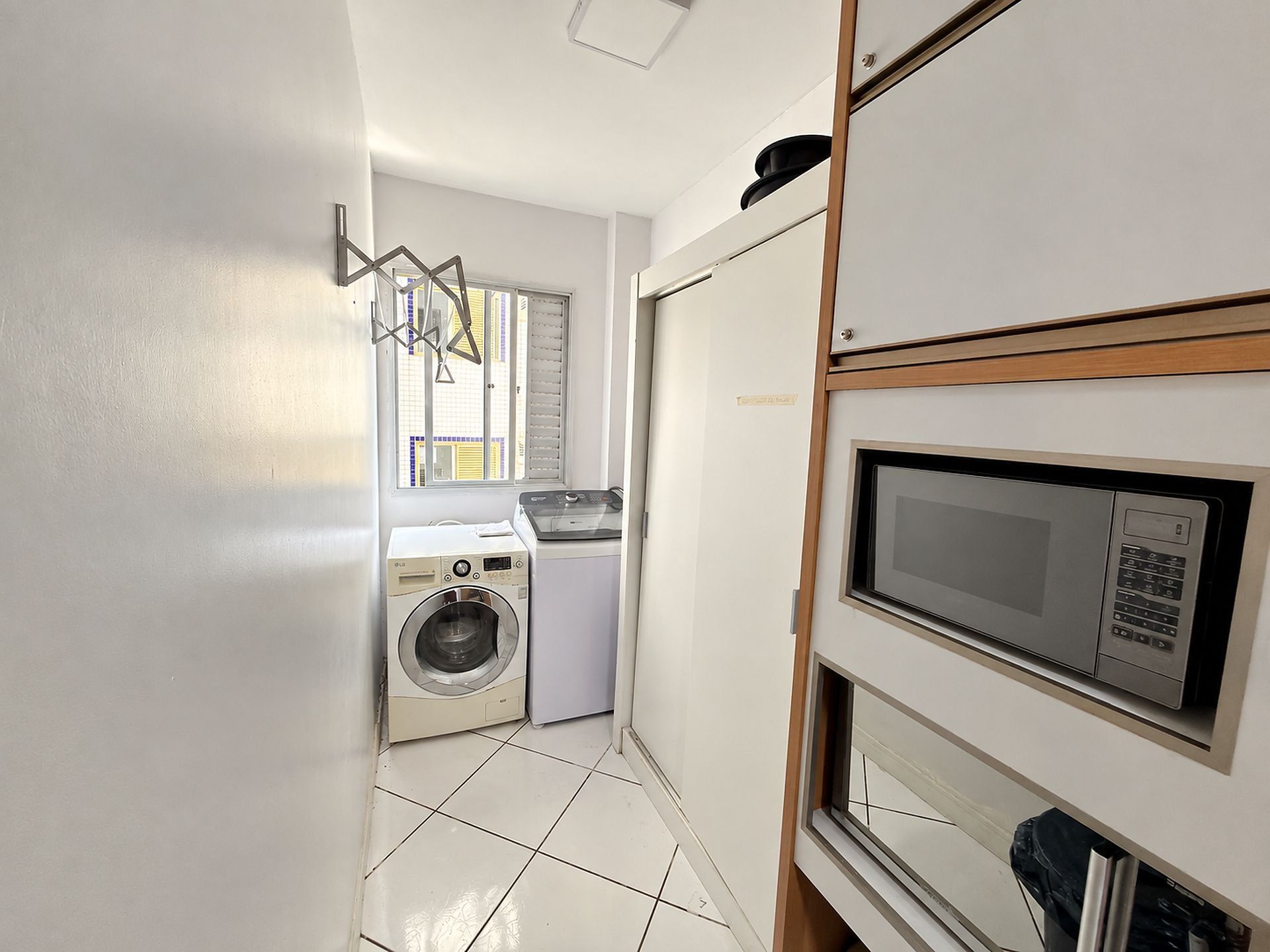 Un espace buanderie équipé d’un lave-linge et d’un sèche-linge, d’un four à micro-ondes et d’une fenêtre avec des stores.
