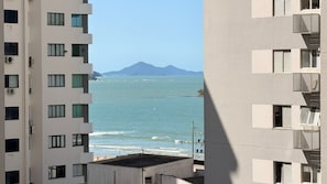 Un edificio alto con múltiples balcones que dan a un mar tranquilo y montañas lejanas.