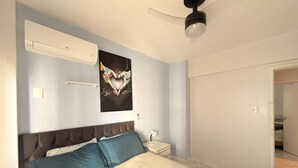 A bedroom with a bed, a ceiling fan, an air conditioning unit, a wall-mounted artwork, and a door leading to another room. - Republica Argentina (Balneário Camboriú)