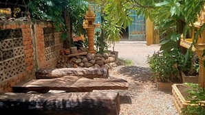 A garden pathway with a brick wall, wooden logs, and a decorative pillar. - Siem Reap Local Stay (Siem Reap)