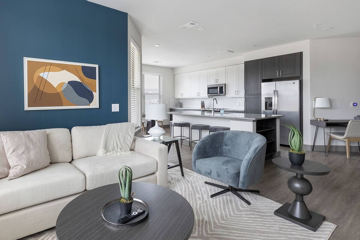 A modern living room with a sofa, armchairs, a coffee table, and a kitchen in the background.