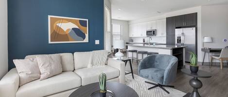 A modern living room with a sofa, armchairs, a coffee table, and a kitchen in the background.