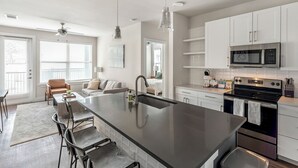 A modern kitchen with a central island, stainless steel appliances, and a dining area with bar stools. - Landing Apartments near UT San Antonio (San Antonio)