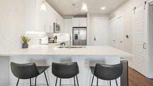 A modern kitchen with white cabinetry, a large island with bar stools, stainless steel appliances, and pendant lighting. - Landing Apartments near UT San Antonio (San Antonio)