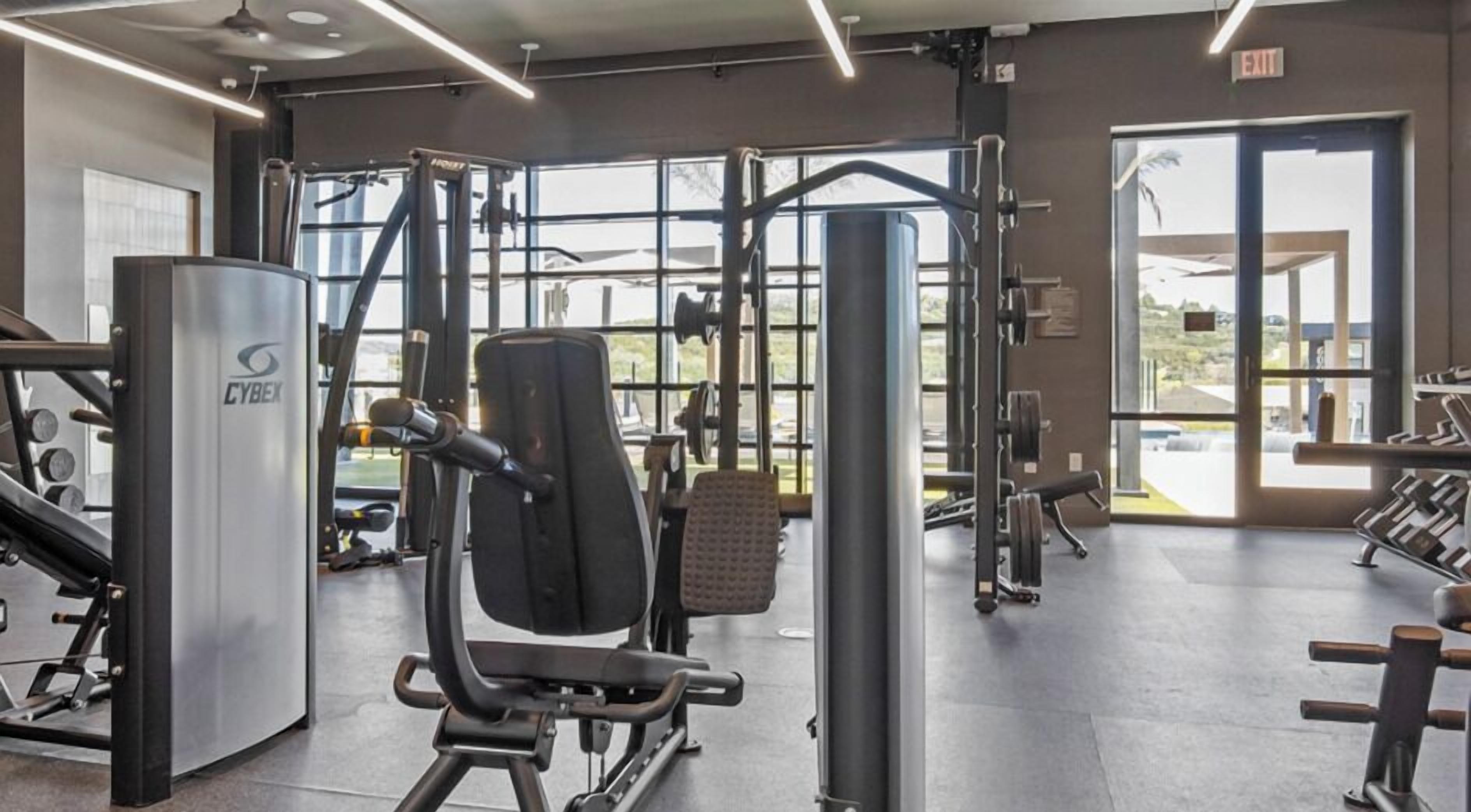 A gym with various exercise equipment, large windows, and an exit sign.
