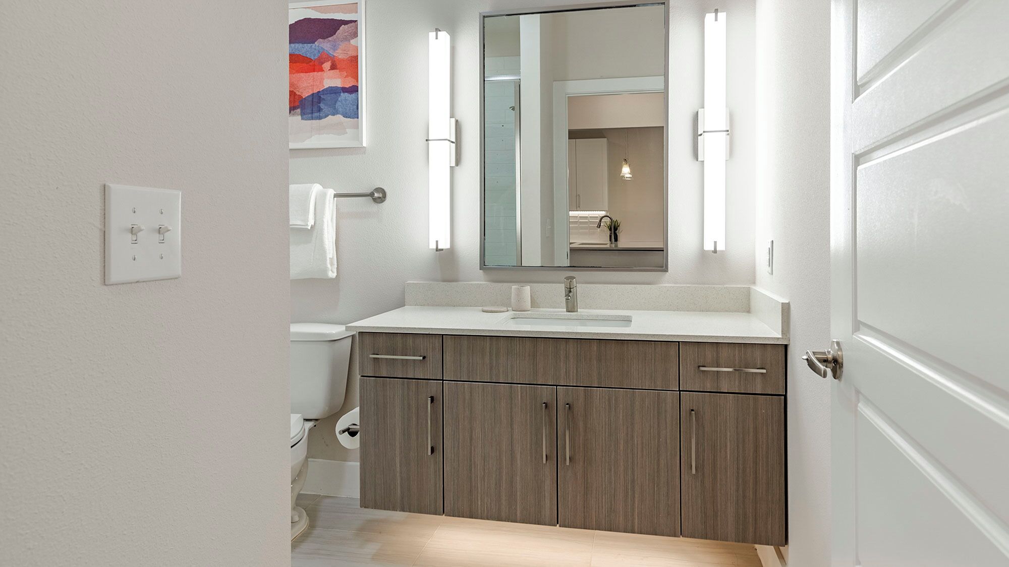 Een moderne badkamer met een witte wastafel, een grote spiegel en een toilet.