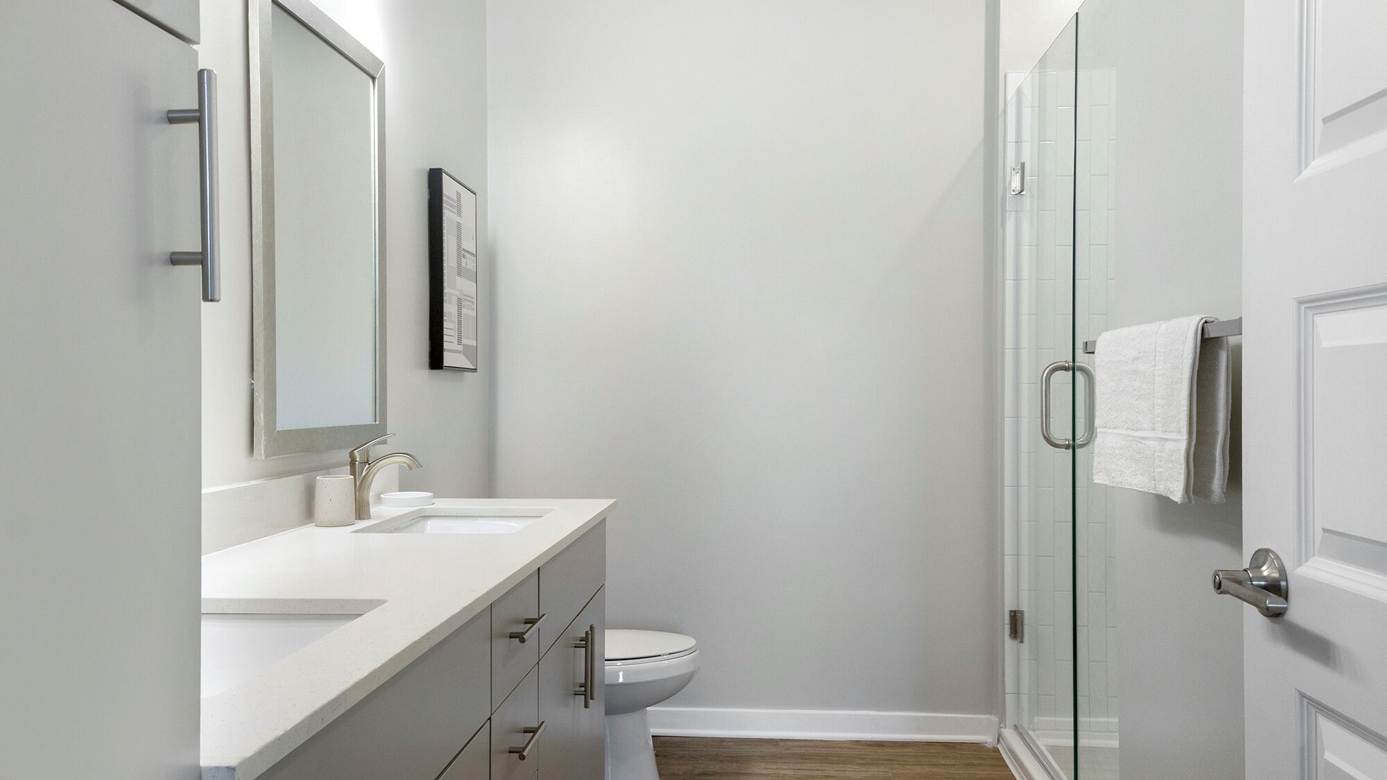 Een moderne badkamer met een witte wastafel, spiegel en toilet, en een douchecabine met glazen deur.