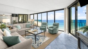 A spacious living room with a large window overlooking the beach, a sofa set, and a coffee table.