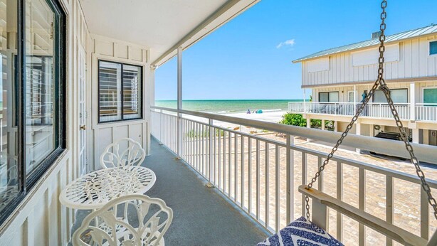 Ein Balkon mit Blick auf den Strand, weiße Gartenmöbel und einem Hängesessel.