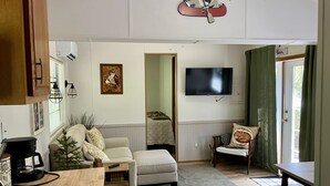A living room with a sofa, a coffee table, a TV mounted on the wall, and a dining area with a table and chairs.
