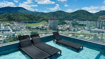 A rooftop infinity pool with lounge chairs and a cityscape view.