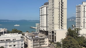 A high-rise building with multiple balconies, a view of the sea, and a distant city skyline. - Manhattan Flats (Itapema)