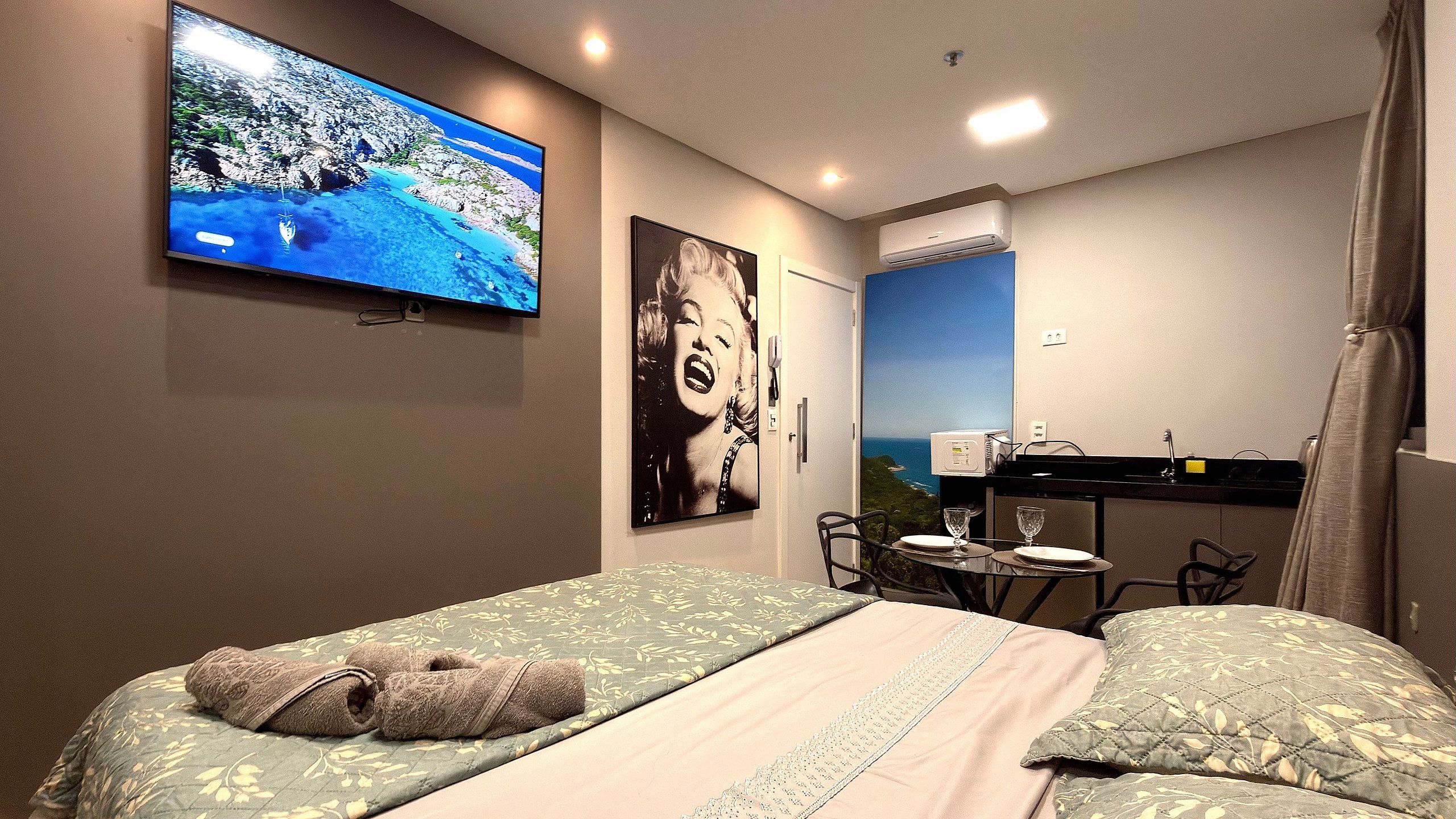 Une chambre d’hôtel avec un lit, une télévision, une affiche, un bureau avec une chaise et une vue sur la mer.