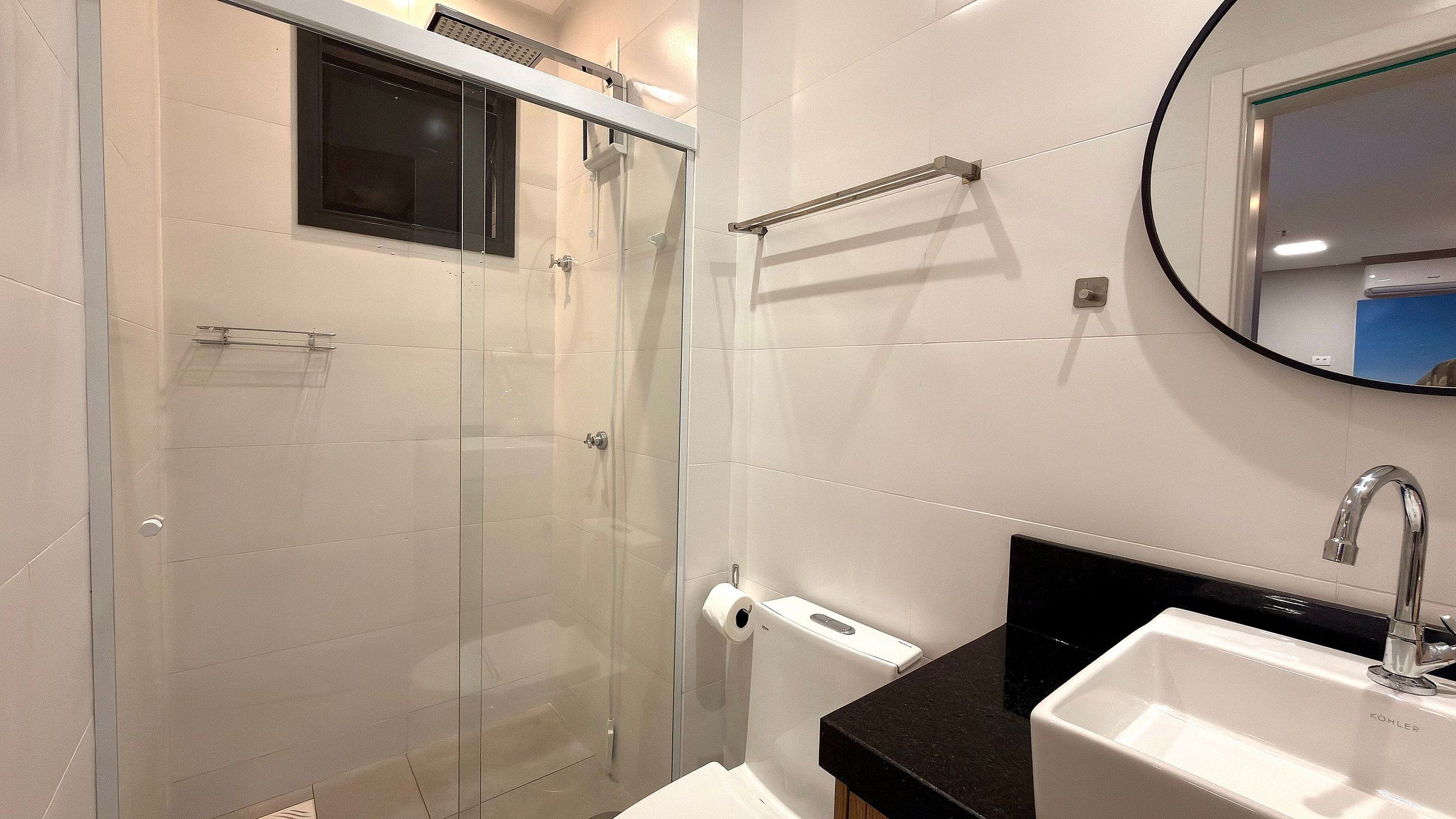 Un baño moderno con cabina de ducha de vidrio, lavabo con encimera negra y un espejo.