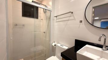 Un baño moderno con cabina de ducha de vidrio, lavabo con encimera negra y un espejo.